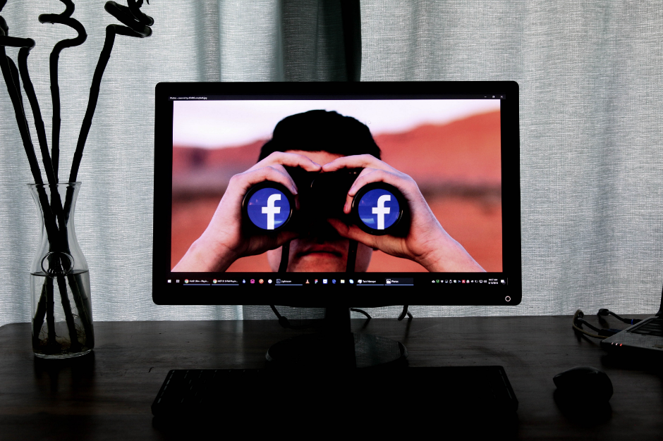 A person looking through binoculars with Facebook logos on a computer screen